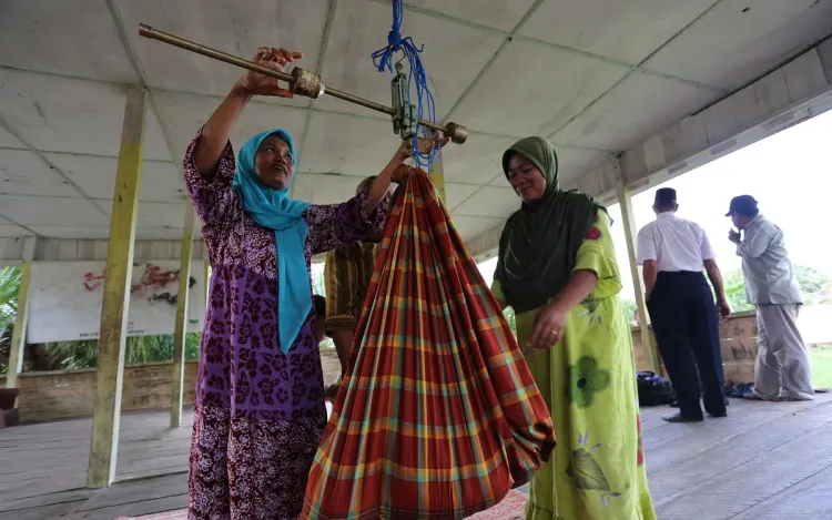 Health volunteers weighing an infant in a sling on a hanging scale, for health programme and tender suppliers