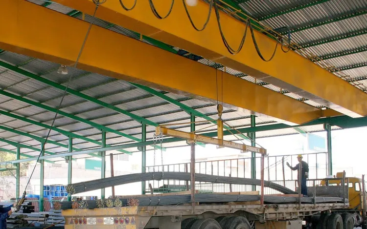 A yellow overhead crane lifting bundles of steel bars onto a trailer, for industrial and logistics companies