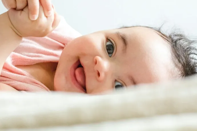baby in pink shirt lying on white textile and smiling